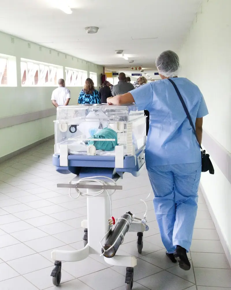Profissional de saúde conduzindo uma incubadora pelo corredor de um hospital